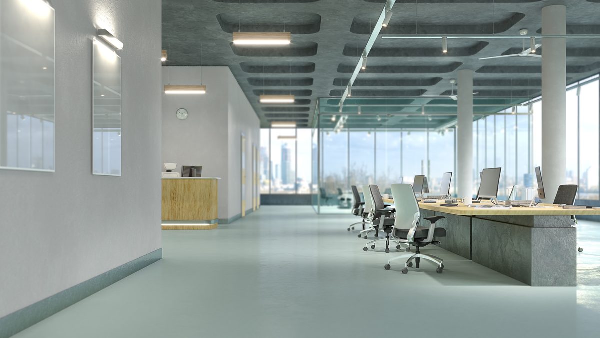 An empty open-plan office with rows of desks and chairs, linear pendant lights and floor-to-ceiling windows looking out over city buildings